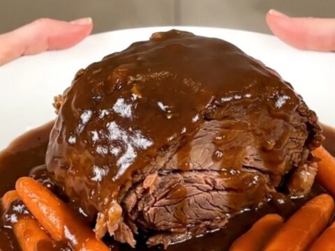 A close-up of a tender Guinness pot roast with glazed carrots and rich gravy on a white plate.