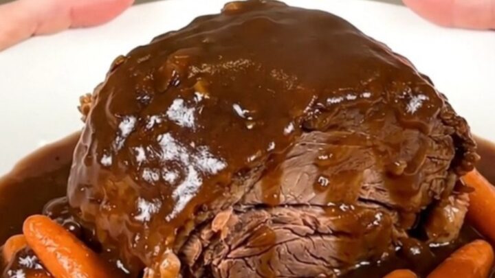 A close-up of a tender Guinness pot roast with glazed carrots and rich gravy on a white plate.
