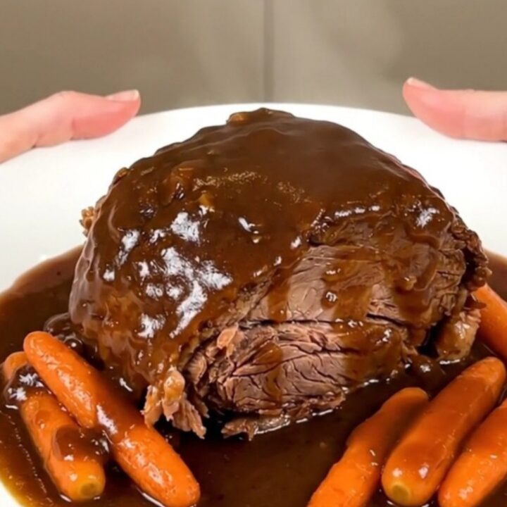 A close-up of a tender Guinness pot roast with glazed carrots and rich gravy on a white plate.