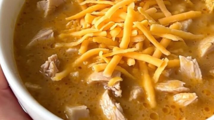 A steaming bowl of creamy chicken taco soup topped with shredded cheddar cheese and crunchy corn chips.
