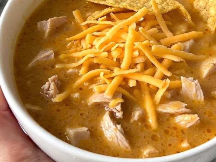 A steaming bowl of creamy chicken taco soup topped with shredded cheddar cheese and crunchy corn chips.