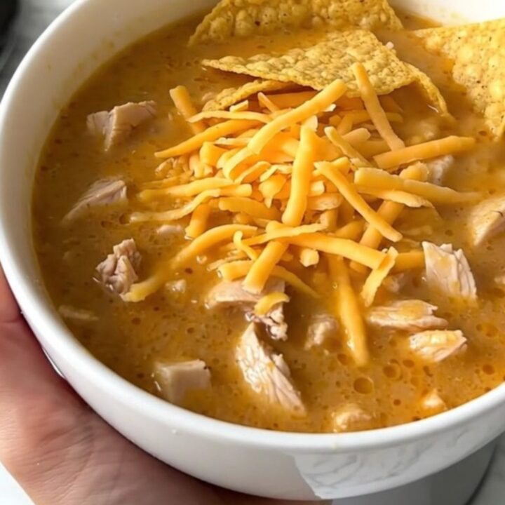 A steaming bowl of creamy chicken taco soup topped with shredded cheddar cheese and crunchy corn chips.
