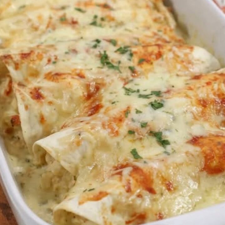 A spatula lifting a steaming creamy white chicken enchilada from a white baking dish showing a long cheese pull.