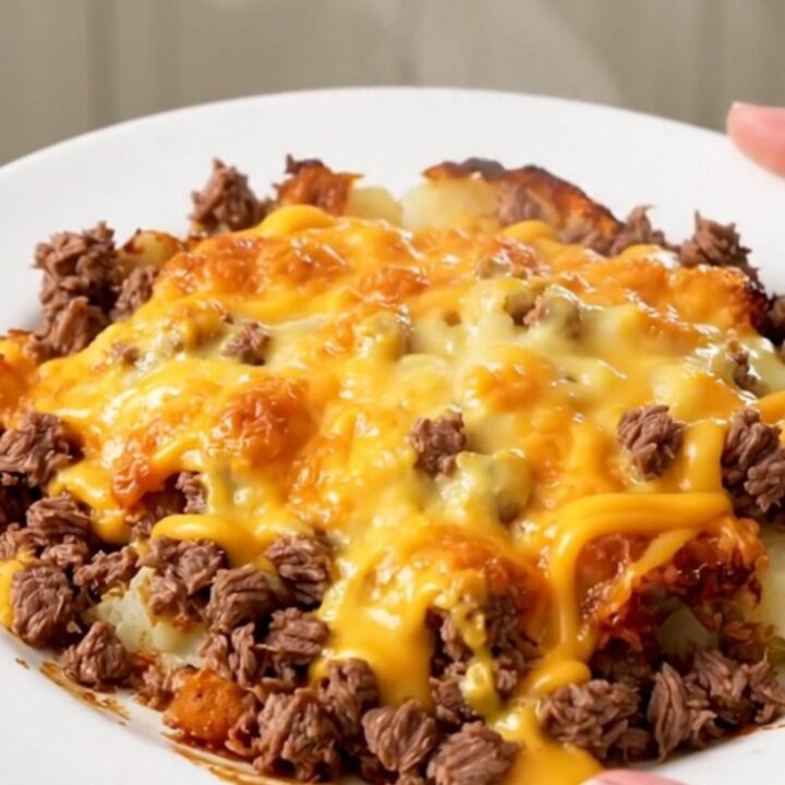 A steaming, glossy cheesy beef and potato casserole served on a white plate, captured in a close-up shot.