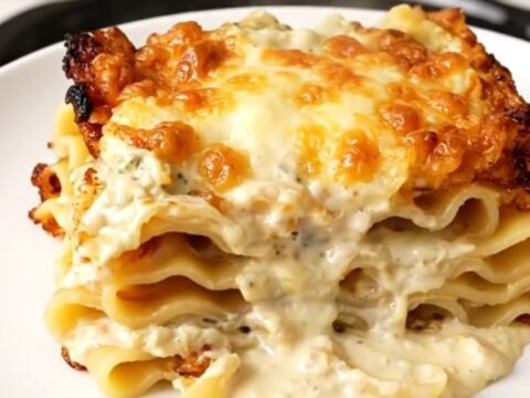 A steaming slice of creamy spinach lasagna on a white plate with a blurred kitchen background.