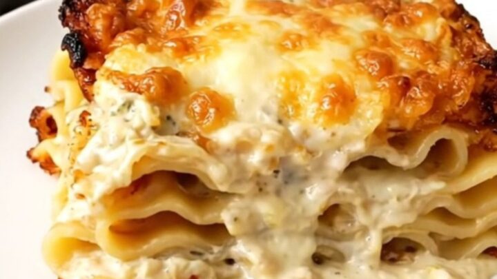 A steaming slice of creamy spinach lasagna on a white plate with a blurred kitchen background.