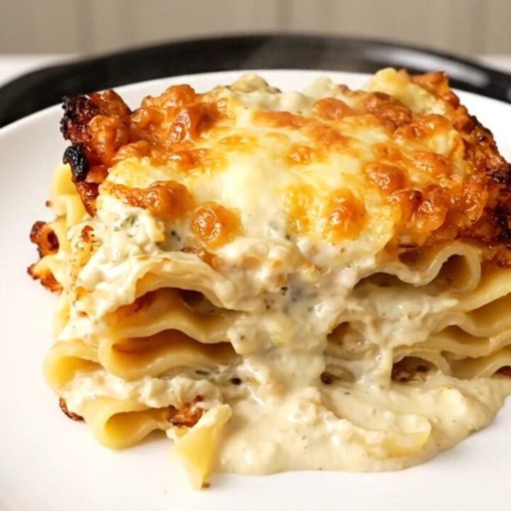 A steaming slice of creamy spinach lasagna on a white plate with a blurred kitchen background.