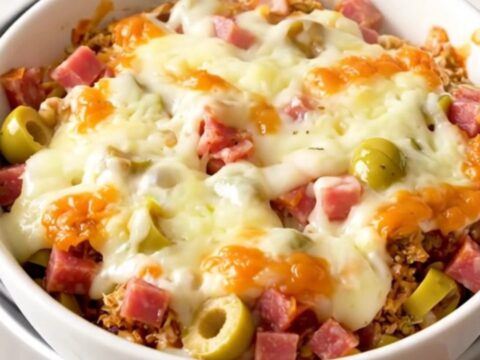 A close-up shot of a warm, creamy muffuletta dip in a white bowl with visible chunks of meat and olives.