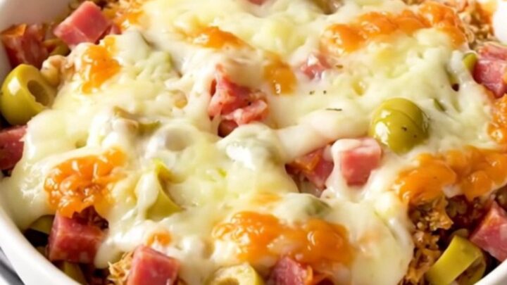 A close-up shot of a warm, creamy muffuletta dip in a white bowl with visible chunks of meat and olives.