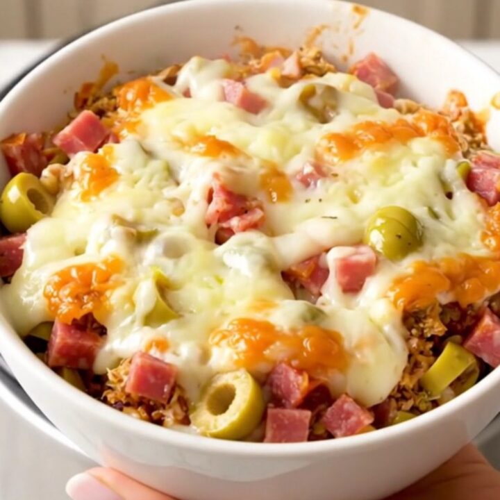 A close-up shot of a warm, creamy muffuletta dip in a white bowl with visible chunks of meat and olives.