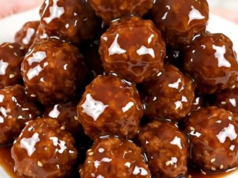 A top-down view of glazed Korean BBQ meatballs in a slow cooker on a white speckled countertop.