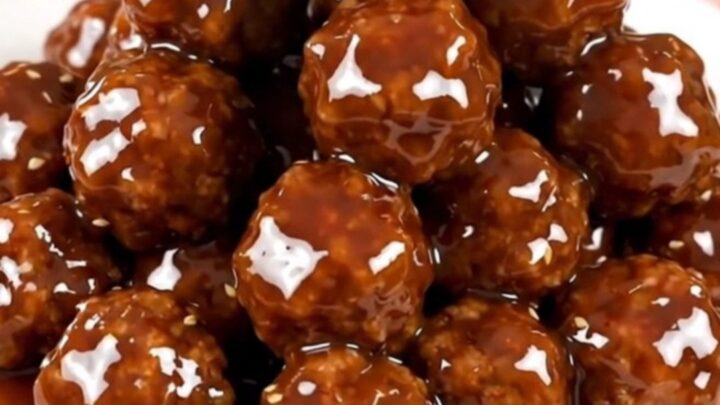 A top-down view of glazed Korean BBQ meatballs in a slow cooker on a white speckled countertop.