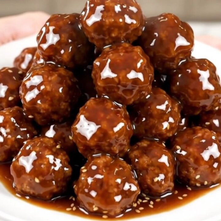 A top-down view of glazed Korean BBQ meatballs in a slow cooker on a white speckled countertop.