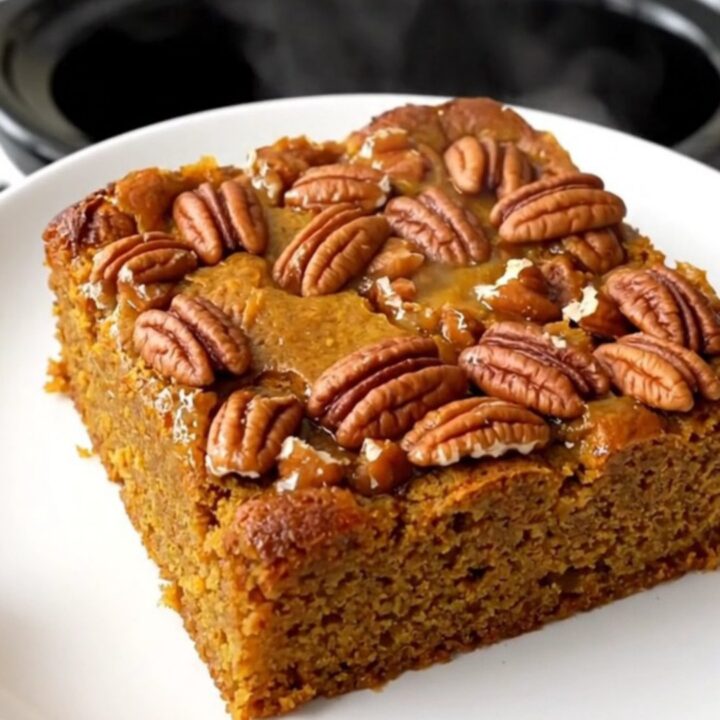 A warm pumpkin praline dump cake in a slow cooker with a golden crunchy pecan topping.