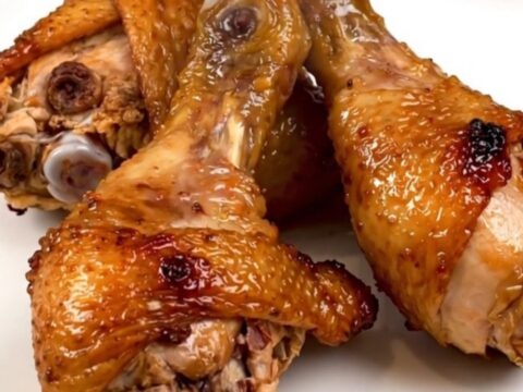 A top-down view of raw chicken drumsticks in a slow cooker topped with diced onions and a golden brown sugar mustard glaze.