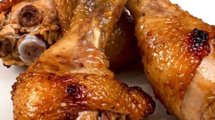 A top-down view of raw chicken drumsticks in a slow cooker topped with diced onions and a golden brown sugar mustard glaze.