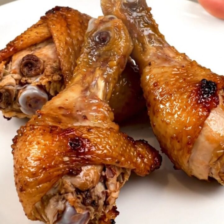 A top-down view of raw chicken drumsticks in a slow cooker topped with diced onions and a golden brown sugar mustard glaze.