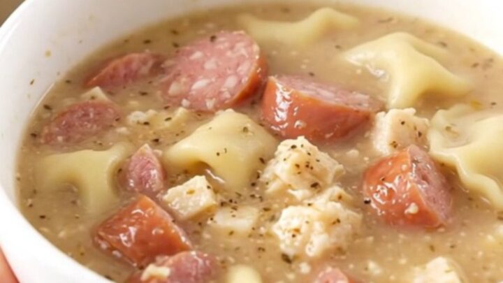 A steaming bowl of creamy pierogi and sausage chowder held by a hand.