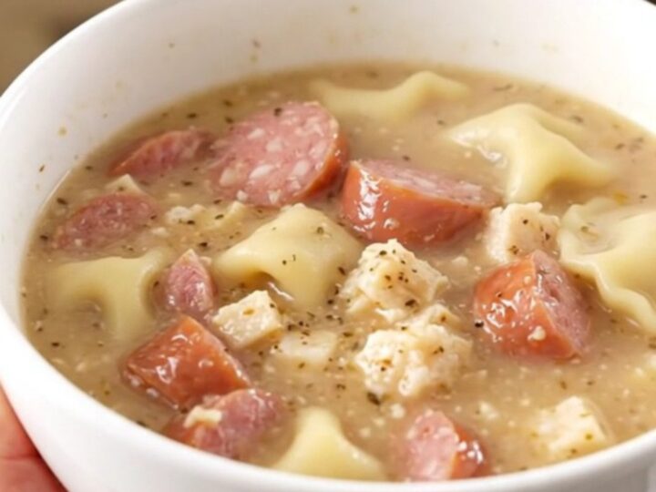 A steaming bowl of creamy pierogi and sausage chowder held by a hand.