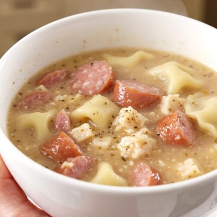 A steaming bowl of creamy pierogi and sausage chowder held by a hand.