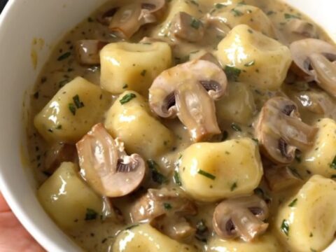 A top-down view of a black slow cooker filled with creamy mushroom herb gnocchi on a white countertop.