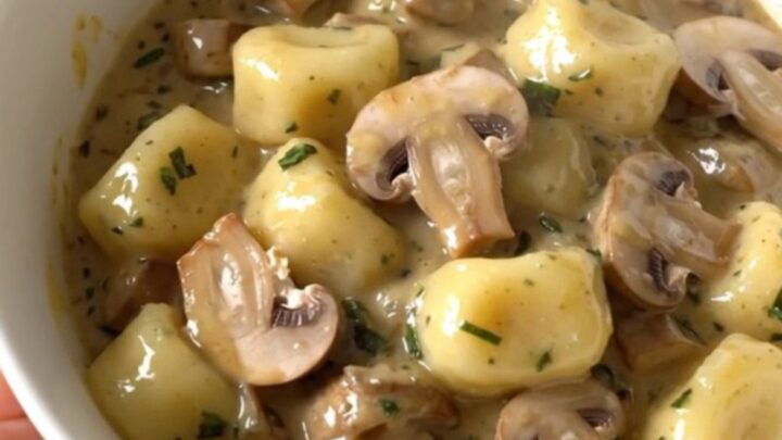 A top-down view of a black slow cooker filled with creamy mushroom herb gnocchi on a white countertop.