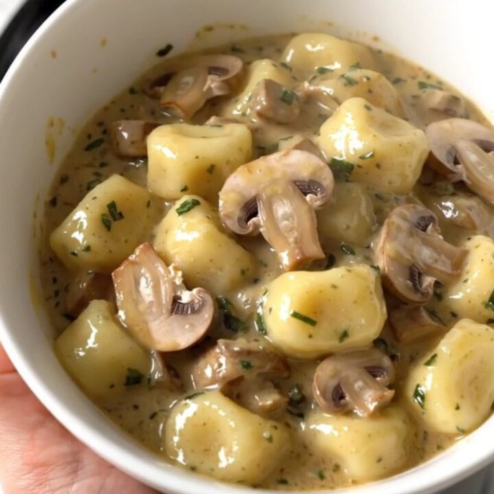 A top-down view of a black slow cooker filled with creamy mushroom herb gnocchi on a white countertop.