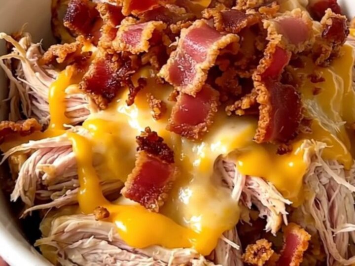 A white bowl filled with creamy shredded chicken, cauliflower florets, and crispy bacon bits.
