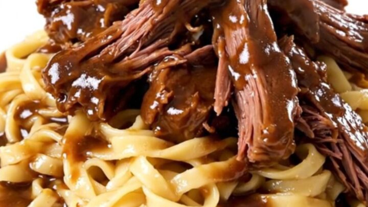 A steaming plate of tender Crockpot Burgundy Beef Tips served over a generous portion of egg noodles.