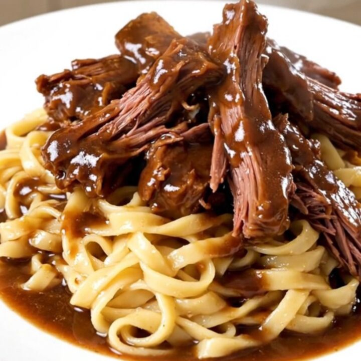 A steaming plate of tender Crockpot Burgundy Beef Tips served over a generous portion of egg noodles.