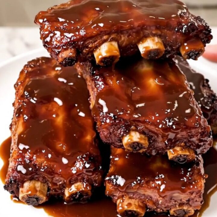 A rack of tender, glazed baby back ribs in a black slow cooker on a speckled countertop.