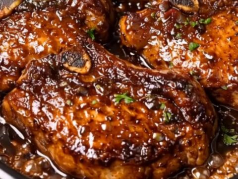 A close-up shot of a bone-in pork chop being basted with a thick, glossy dark garlic soy glaze.