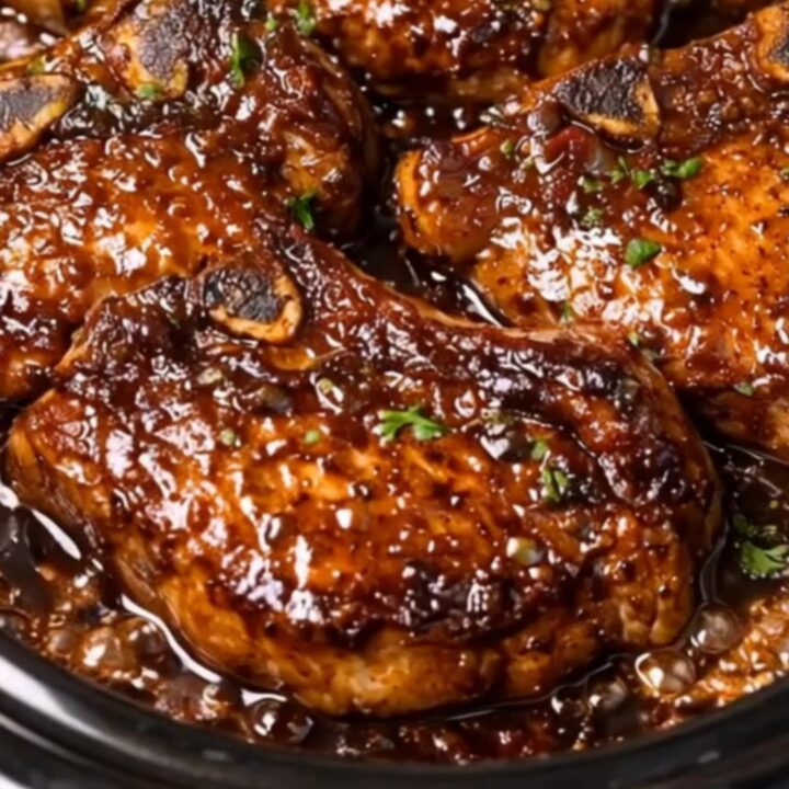 A close-up shot of a bone-in pork chop being basted with a thick, glossy dark garlic soy glaze.