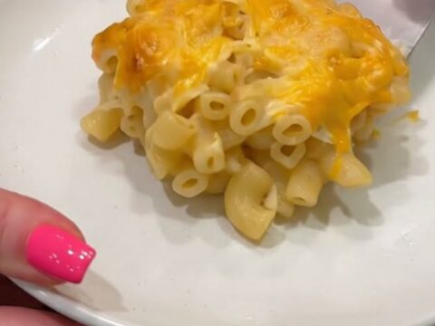 A spatula lifting a portion of baked macaroni and cheese, showcasing a golden cheese pull and bubbling cheddar crust.