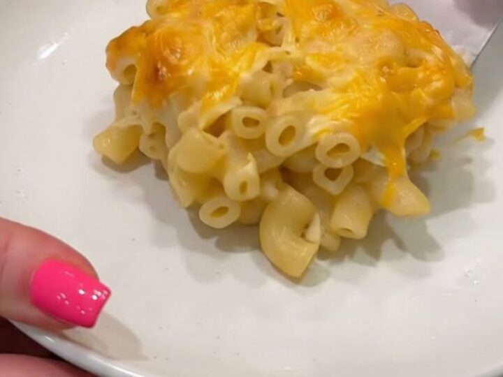 A spatula lifting a portion of baked macaroni and cheese, showcasing a golden cheese pull and bubbling cheddar crust.