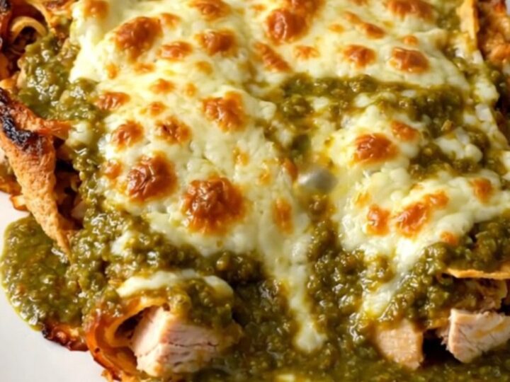 A close-up shot of a slow cooker filled with chicken and green enchilada sauce, topped with melted cheese.