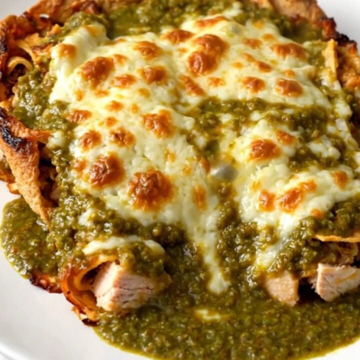 A close-up shot of a slow cooker filled with chicken and green enchilada sauce, topped with melted cheese.