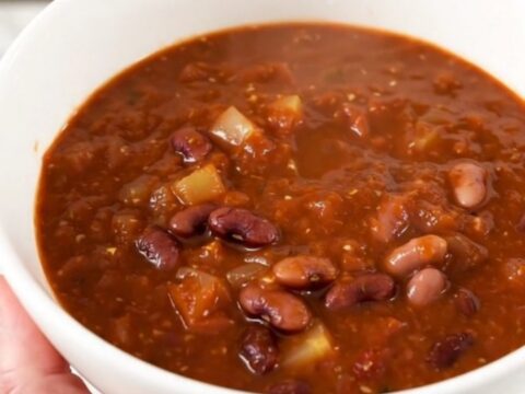 A steaming bowl of Southwest three bean chili served in a white bowl on a kitchen counter.