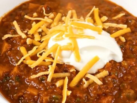 A bowl of steaming ground turkey and sweet potato chili topped with shredded cheddar and sour cream.