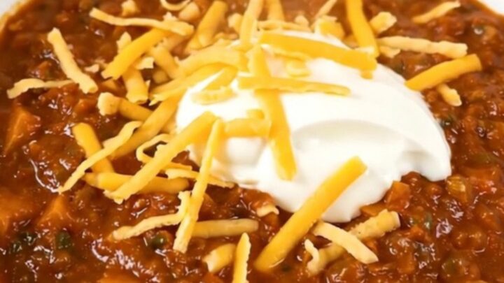 A bowl of steaming ground turkey and sweet potato chili topped with shredded cheddar and sour cream.