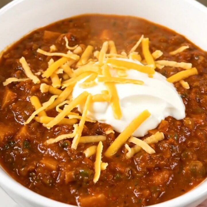 A bowl of steaming ground turkey and sweet potato chili topped with shredded cheddar and sour cream.