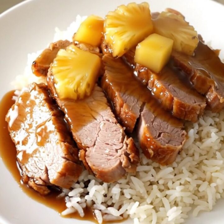 Glazed pineapple teriyaki pork loin sliced on a white plate with rice.