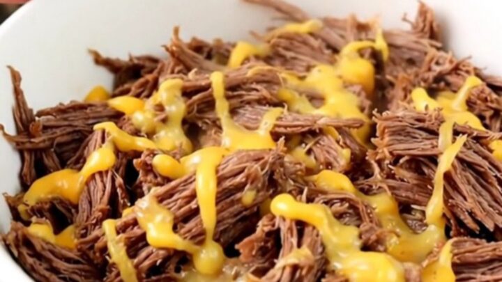 A close-up of tender, shredded beef in a white bowl, showing a glossy texture and steam rising from the meat.