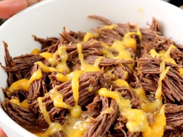 A close-up of tender, shredded beef in a white bowl, showing a glossy texture and steam rising from the meat.