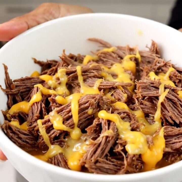 A close-up of tender, shredded beef in a white bowl, showing a glossy texture and steam rising from the meat.