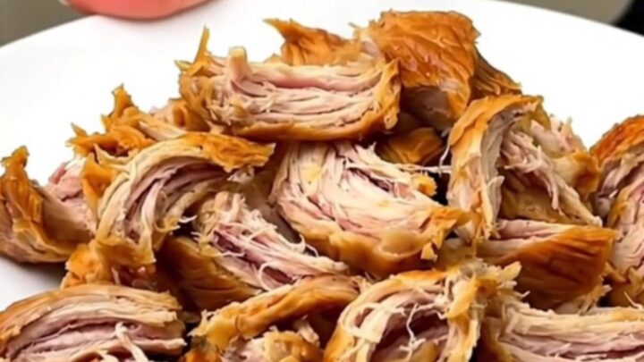 A close-up of shredded Bang Bang Chicken on a white plate with a glossy, creamy orange sauce.