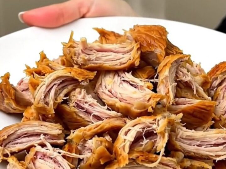 A close-up of shredded Bang Bang Chicken on a white plate with a glossy, creamy orange sauce.