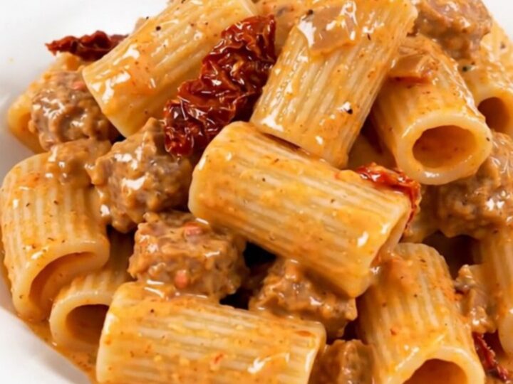 A close-up of creamy rigatoni with Italian sausage and sun-dried tomatoes on a white plate.