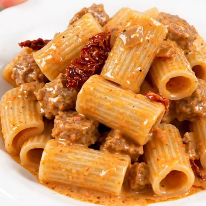 A close-up of creamy rigatoni with Italian sausage and sun-dried tomatoes on a white plate.
