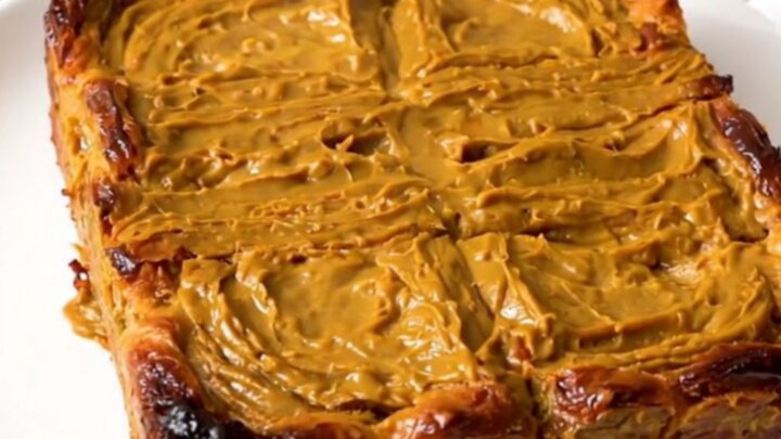 A slow cooker filled with a golden, pumpkin-spiced French toast casserole on a speckled quartz countertop.